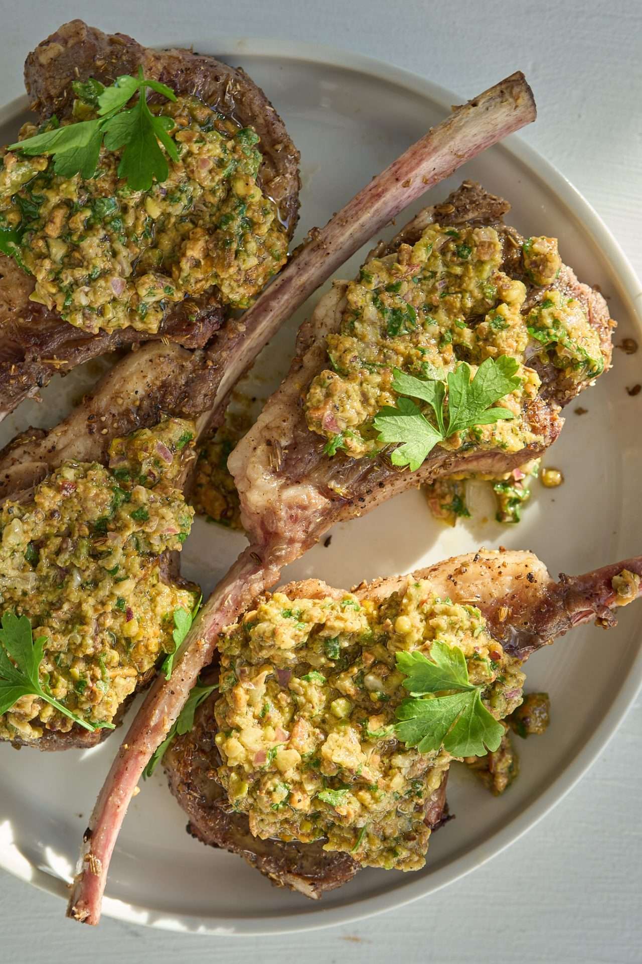 Fennel seed crusted American lamb rack chops topped with pistachio chimichurri on a serving platter