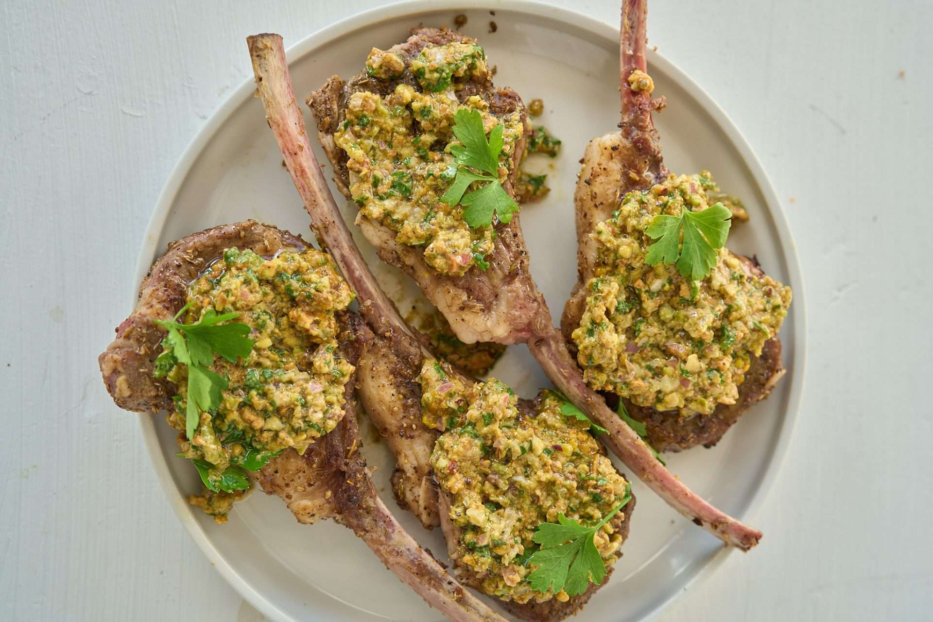 Fennel seed crusted American lamb rack chops topped with pistachio chimichurri on a serving platter