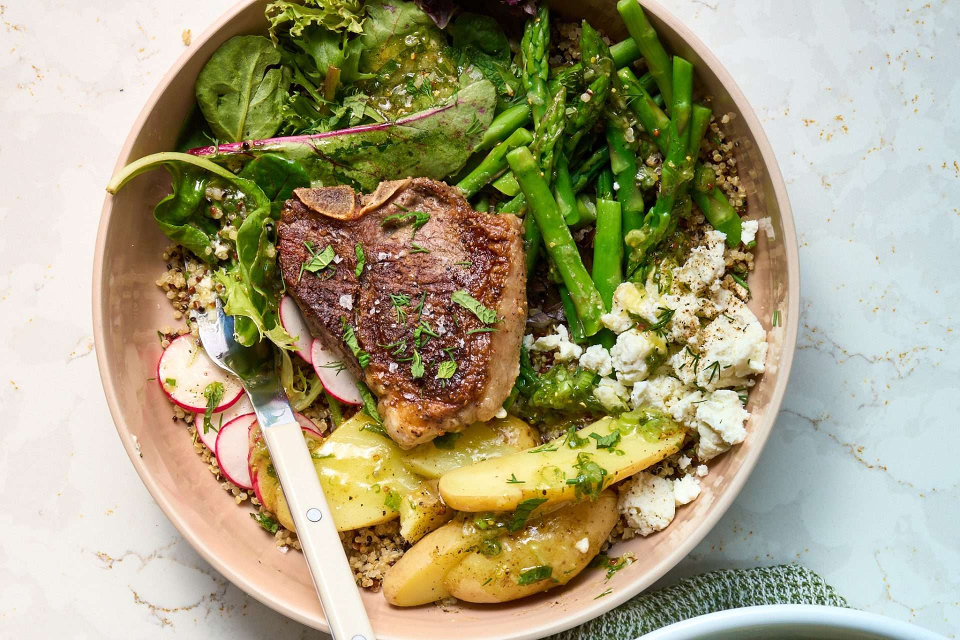Spring veggie bowl with grilled American lamb loin chops, featuring sliced lamb over quinoa with asparagus, leafy greens, radishes, potatoes, herbs, and a light vinaigrette.