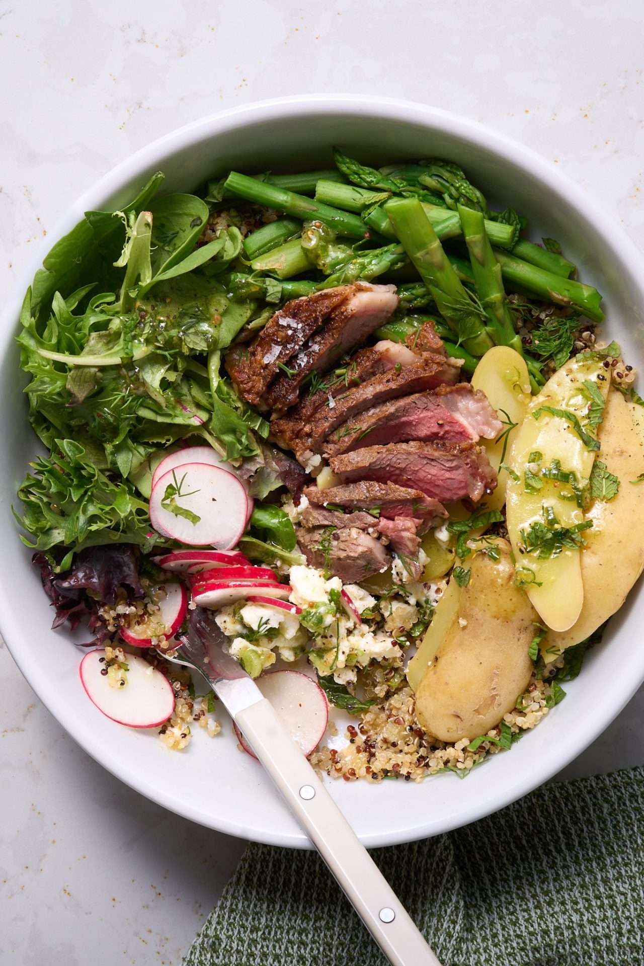 Spring veggie bowl with grilled American lamb loin chops, featuring sliced lamb over quinoa with asparagus, leafy greens, radishes, potatoes, herbs, and a light vinaigrette.