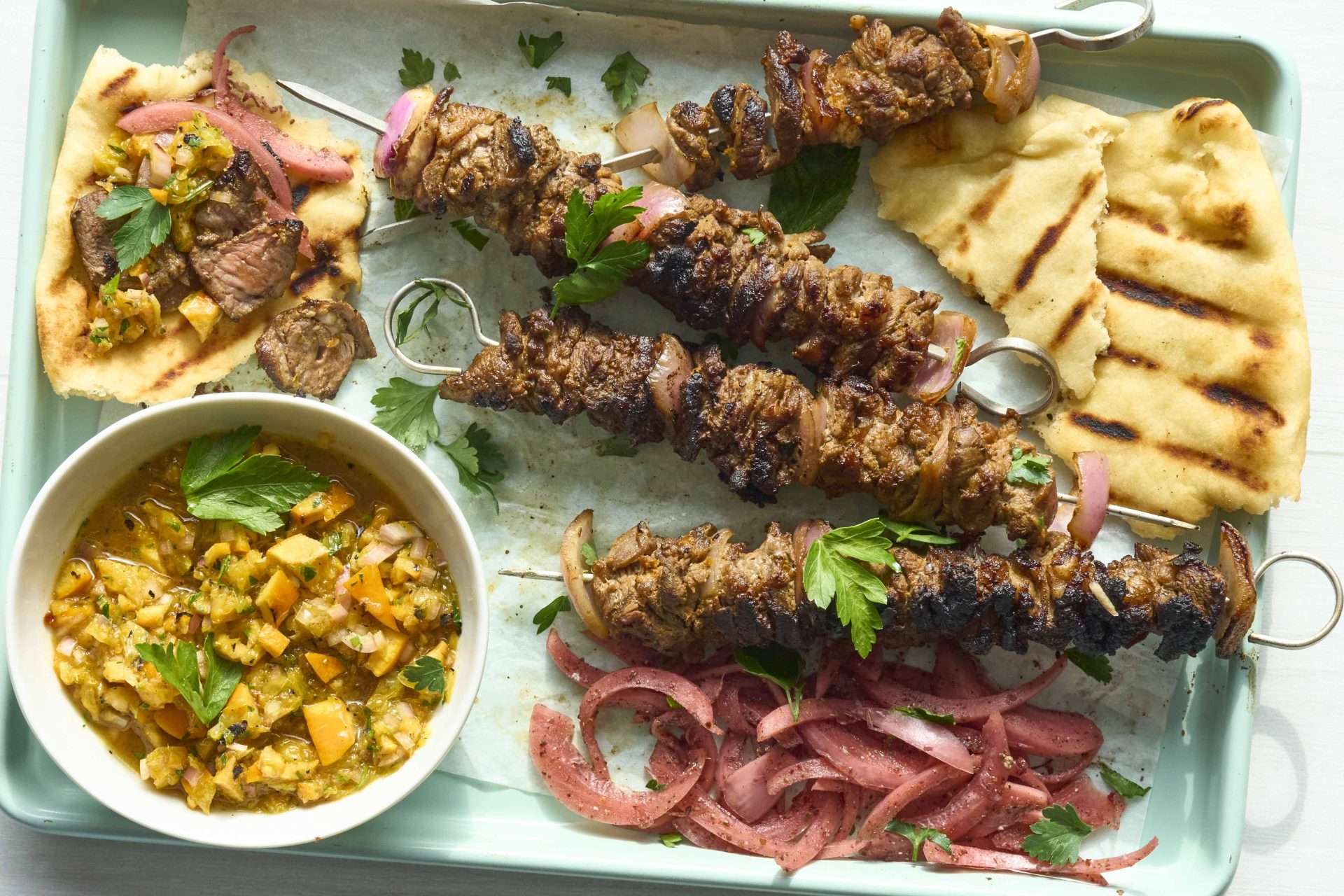 Sheet pan American lamb fajitas served on a warm tortilla with sautéed peppers and onions, sliced lamb, avocado, jalapeños, cilantro, and crumbled cheese, with lime wedges on the side.