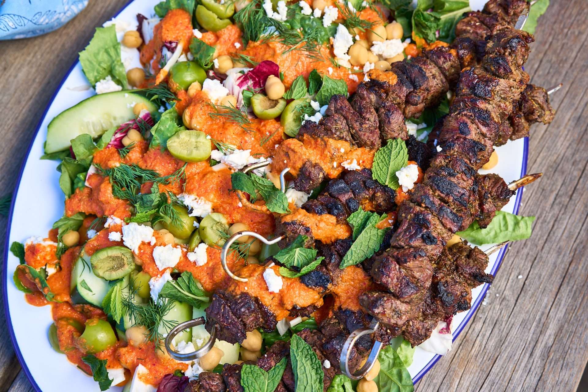 Sheet pan American lamb fajitas served on a warm tortilla with sautéed peppers and onions, sliced lamb, avocado, jalapeños, cilantro, and crumbled cheese, with lime wedges on the side.