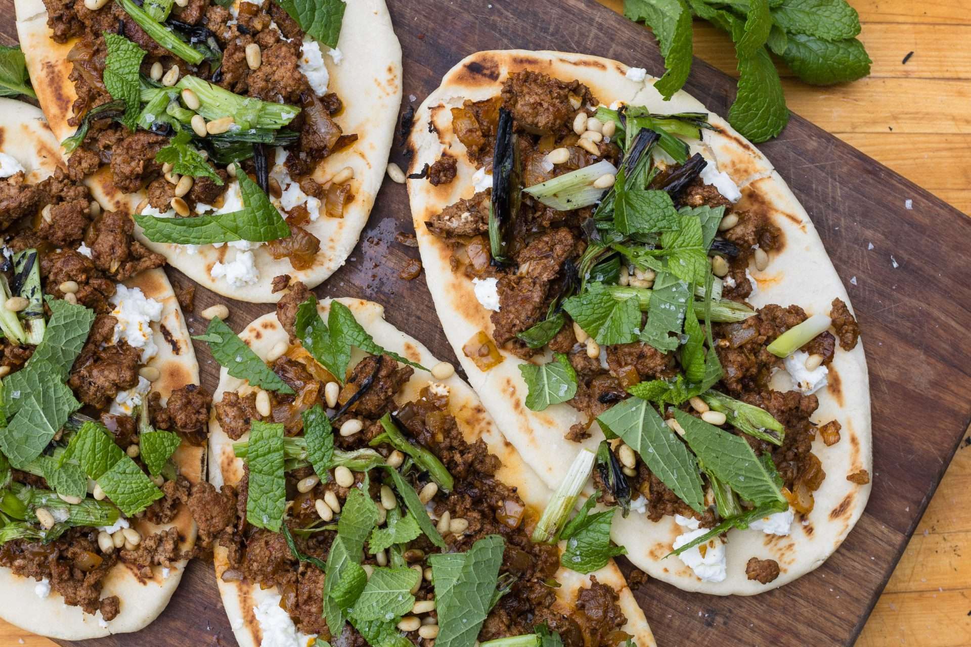 Sheet pan American lamb fajitas served on a warm tortilla with sautéed peppers and onions, sliced lamb, avocado, jalapeños, cilantro, and crumbled cheese, with lime wedges on the side.