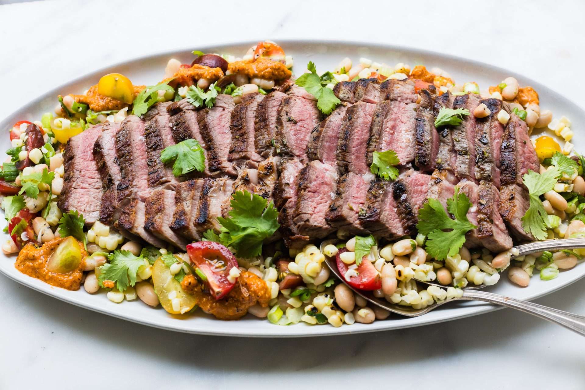 Sheet pan American lamb fajitas served on a warm tortilla with sautéed peppers and onions, sliced lamb, avocado, jalapeños, cilantro, and crumbled cheese, with lime wedges on the side.