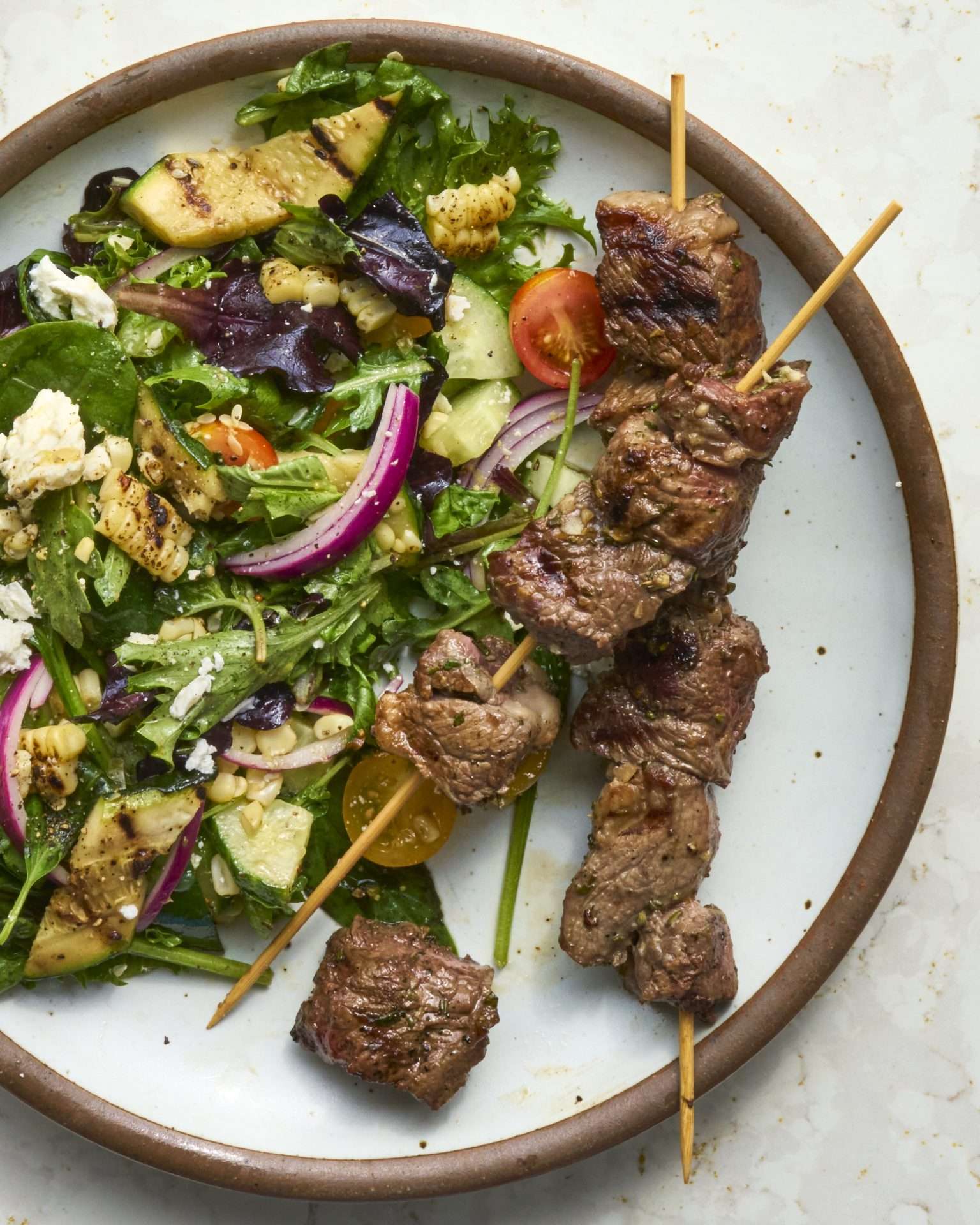 Sheet pan American lamb fajitas served on a warm tortilla with sautéed peppers and onions, sliced lamb, avocado, jalapeños, cilantro, and crumbled cheese, with lime wedges on the side.